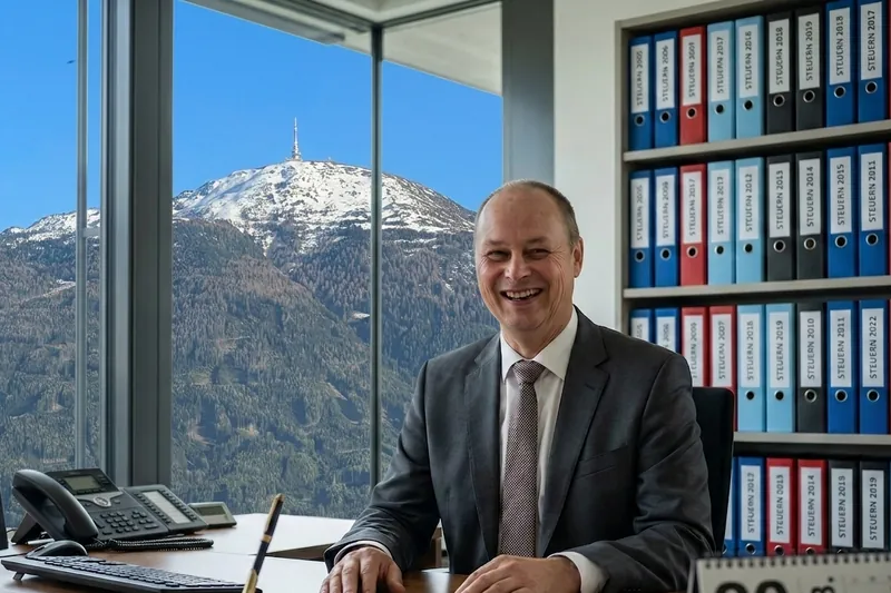 Mag. Edmund Hueber am Schreibtisch in seinem Büro, durch das Fenster der Patscherkofel.